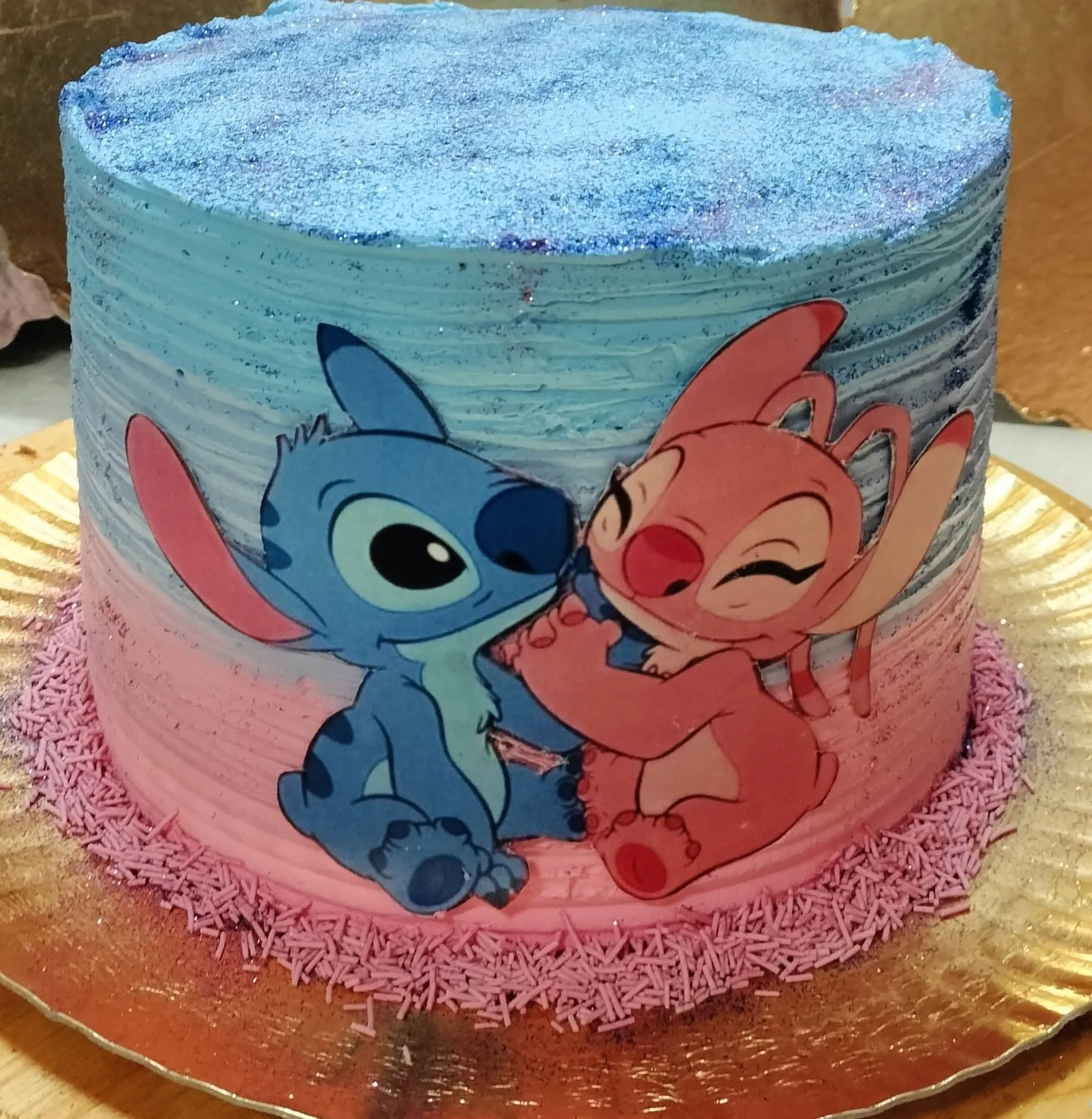 Bolo de aniversário com o Stitch e a Angel, cobertura azul e rosa com brilhos